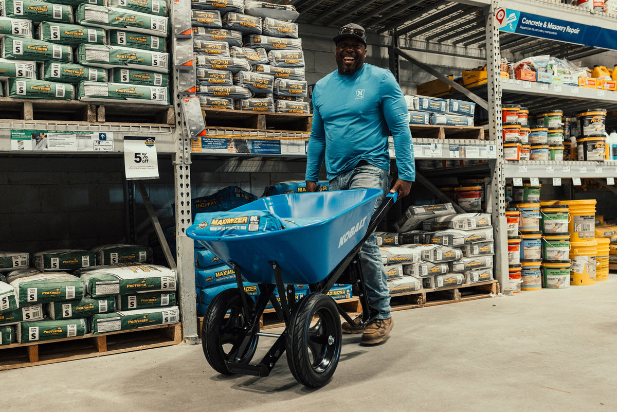 Construction worker pushing a wheelbarrow loaded with concrete mix through a building supply store.