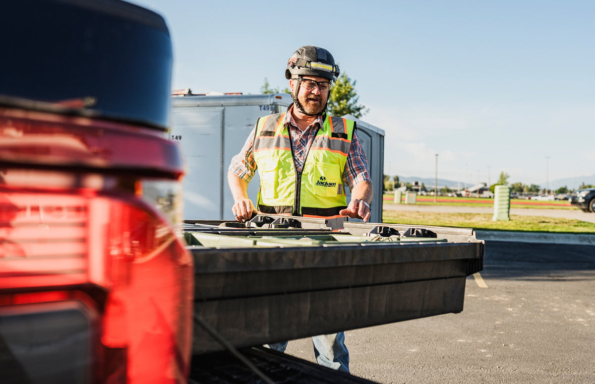 Construction worker in safety gear opens a DECKED Drawer System in the bed of a red pickup truck.