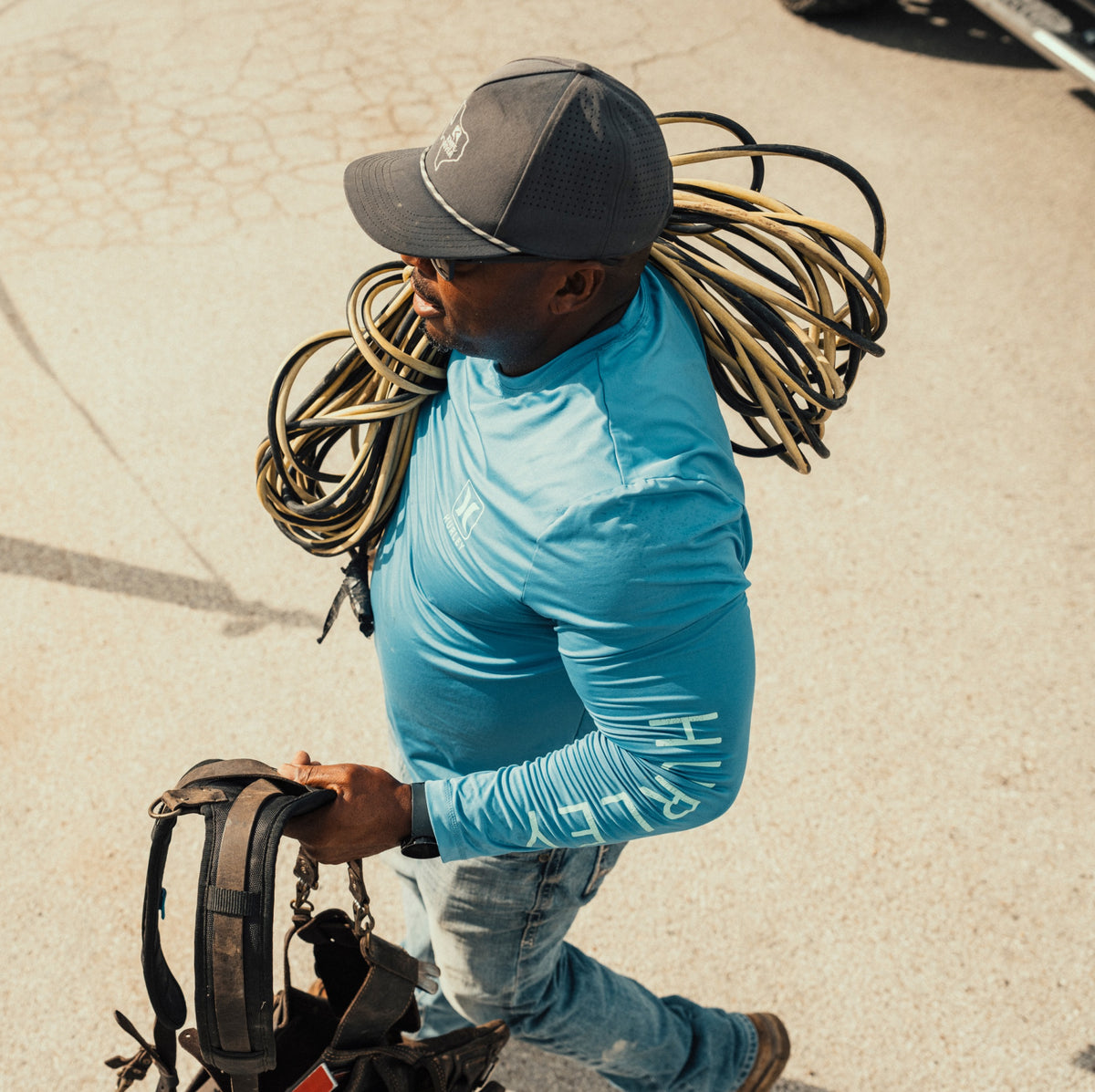 Construction worker carrying coiled power cords and a tool belt across a concrete jobsite.