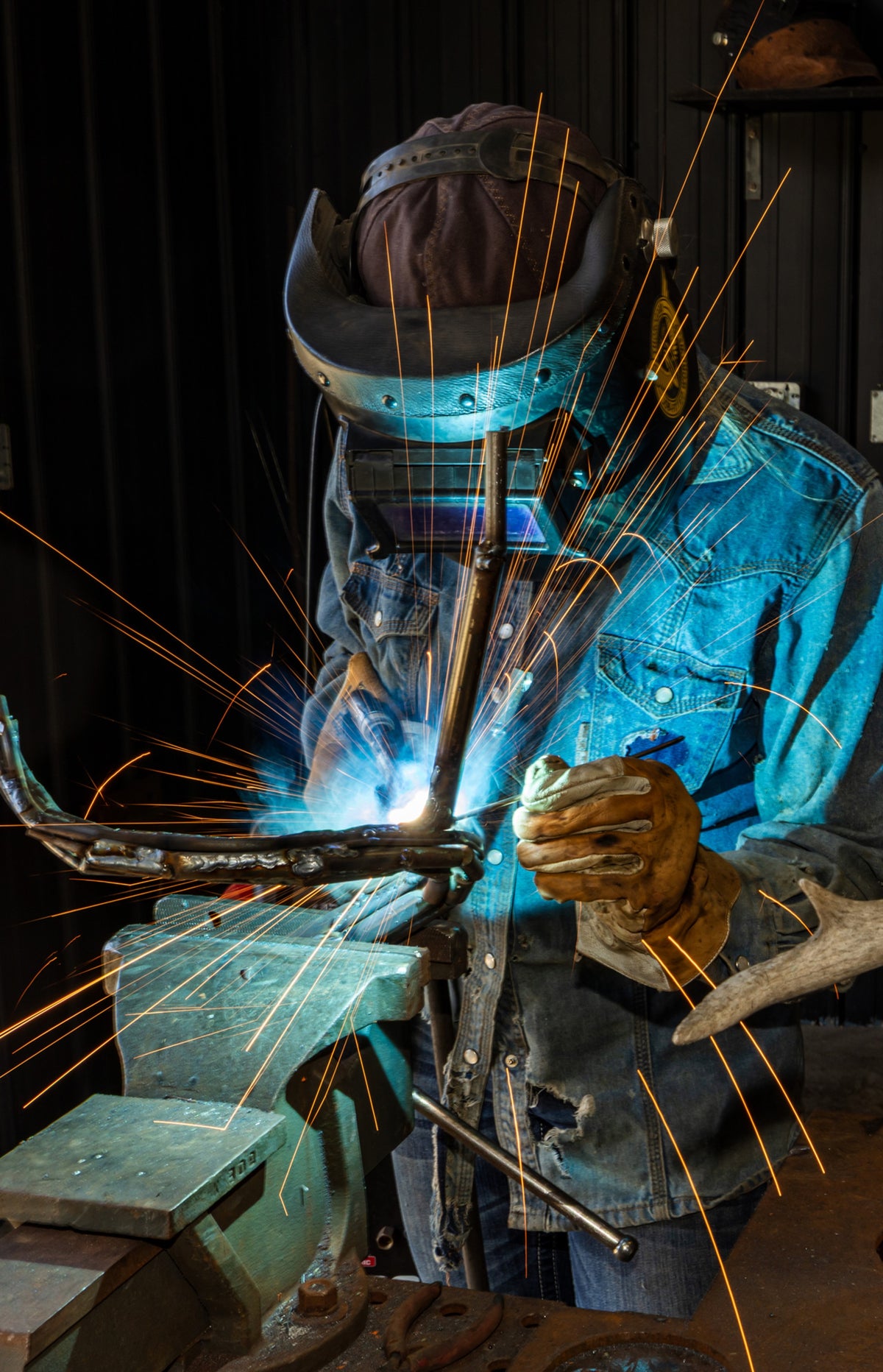 Welder wearing a protective helmet and gloves joins metal pieces as bright sparks fly.