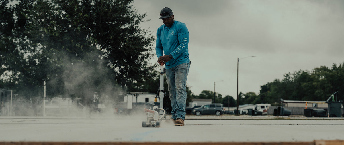 Construction worker operating a concrete saw as dust rises from the jobsite.