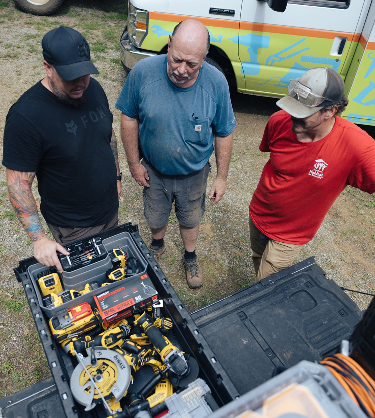 Three crew members look into an open DECKED truck drawer stocked with power tools and supplies.