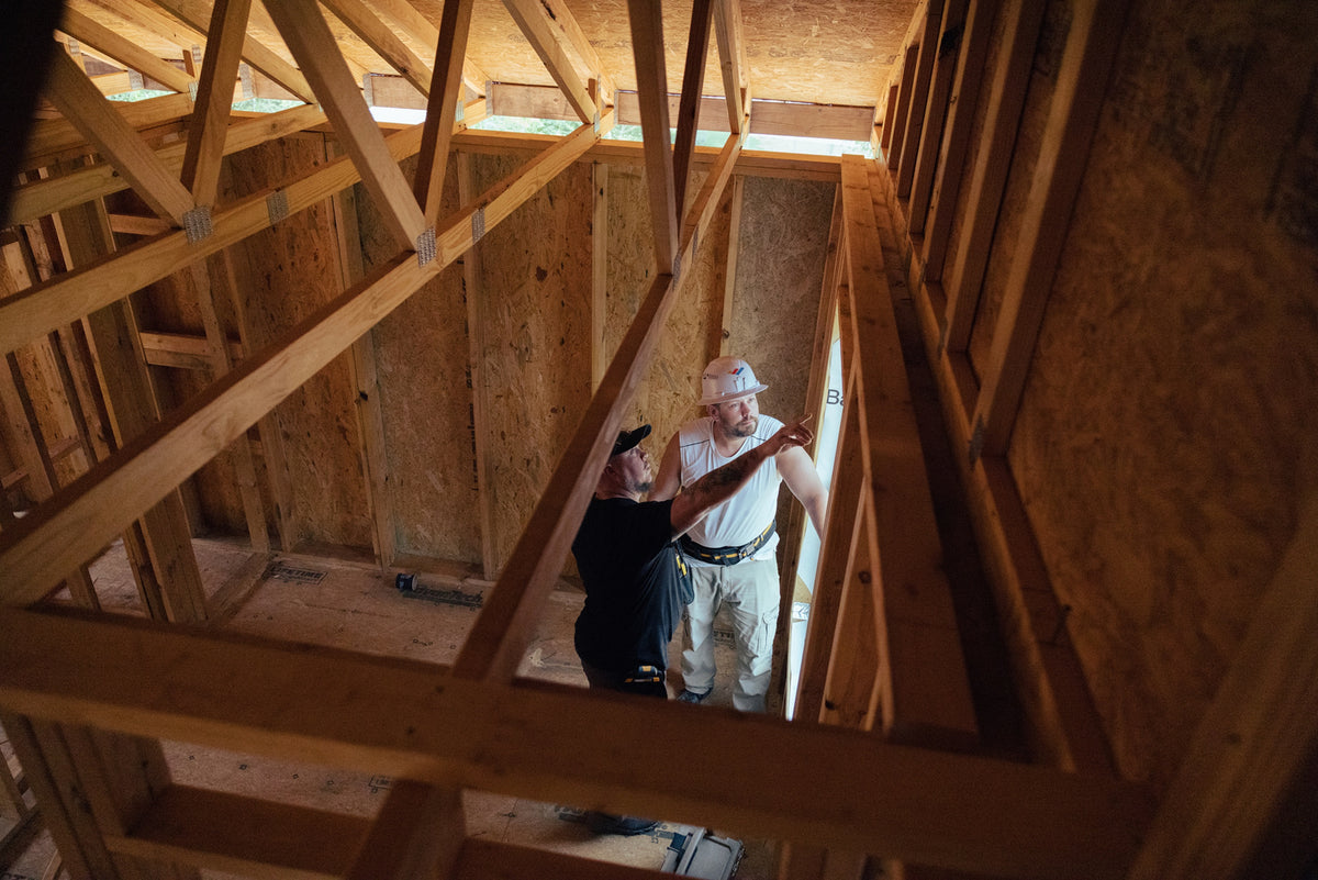 Grid Bottom RightTwo builders discuss the wall framing inside a house under construction.