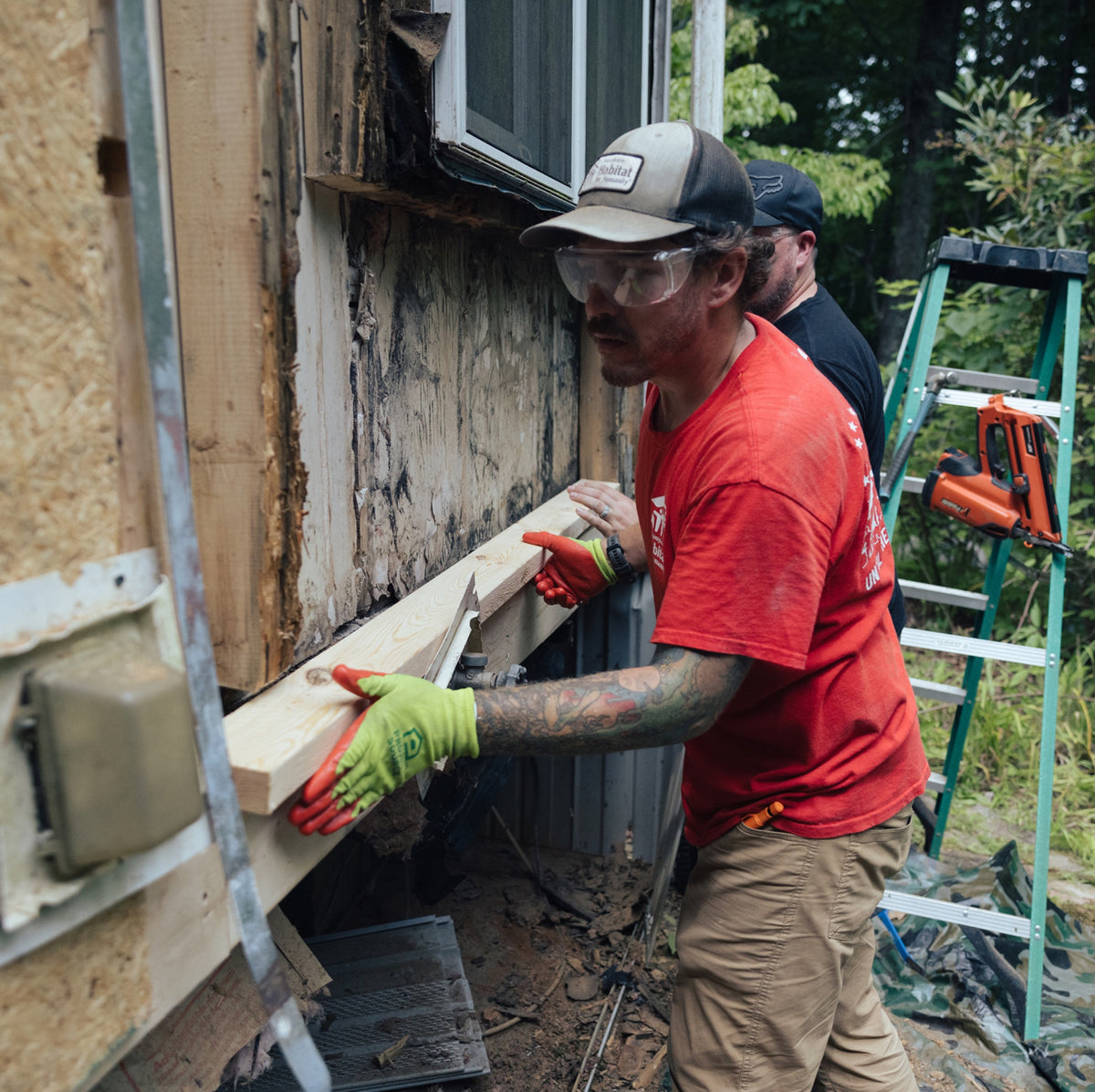 Two crew members position a new board beneath a window during an exterior home repair.