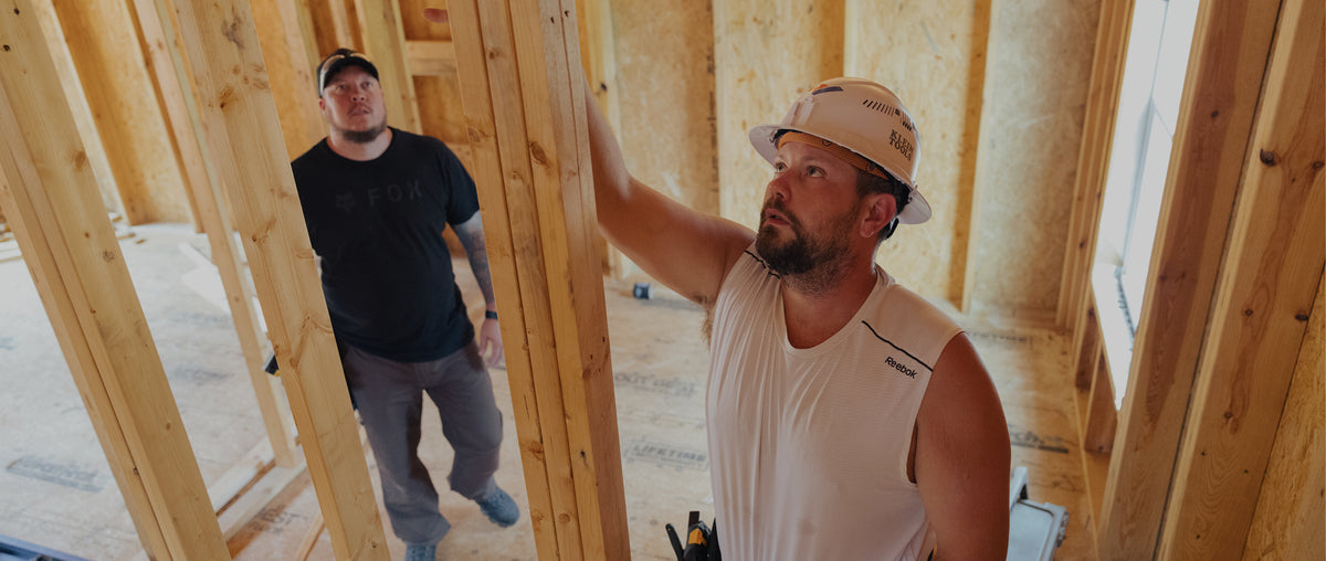 Two builders inspect the wood framing inside a house under construction.