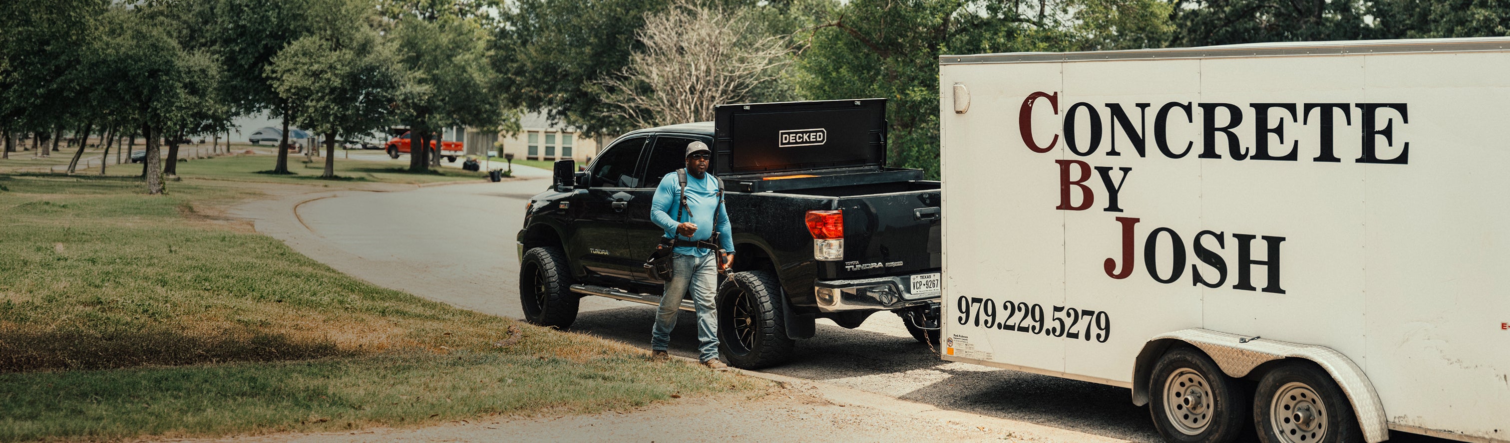 Concrete contractor standing beside a pickup equipped with a DECKED Tool Box and towing a work trailer.