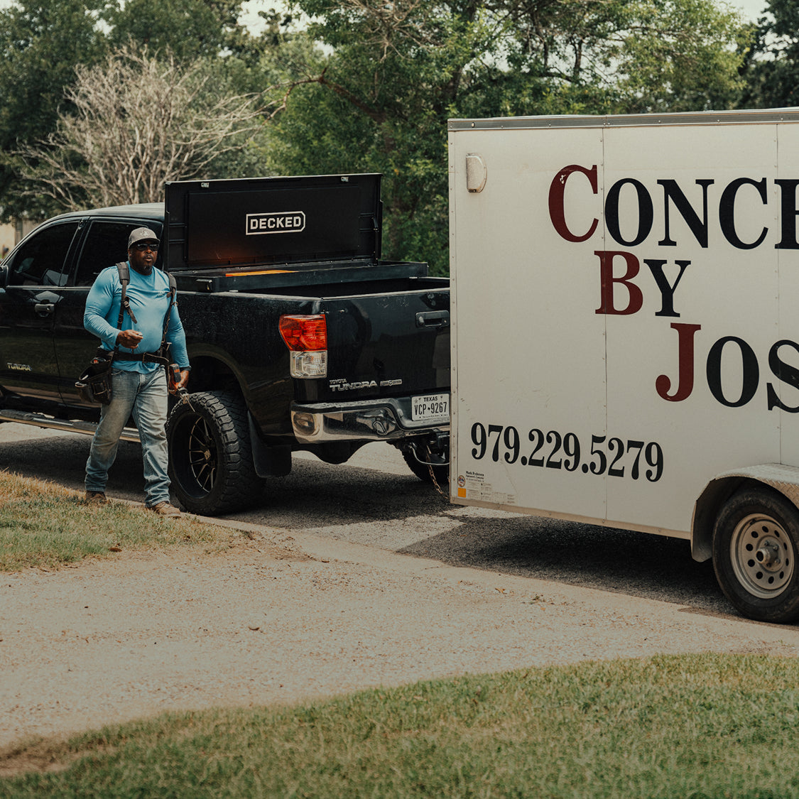 Concrete contractor standing beside a pickup equipped with a DECKED Tool Box and towing a work trailer.