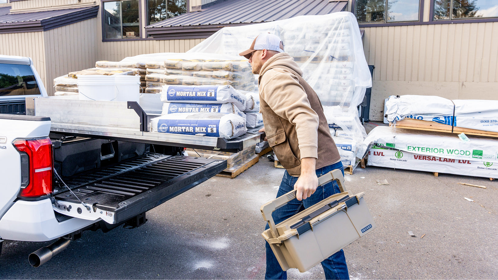 Contractor carrying a DECKED sixer beside a CargoGlide loaded with bags of mortar mix.