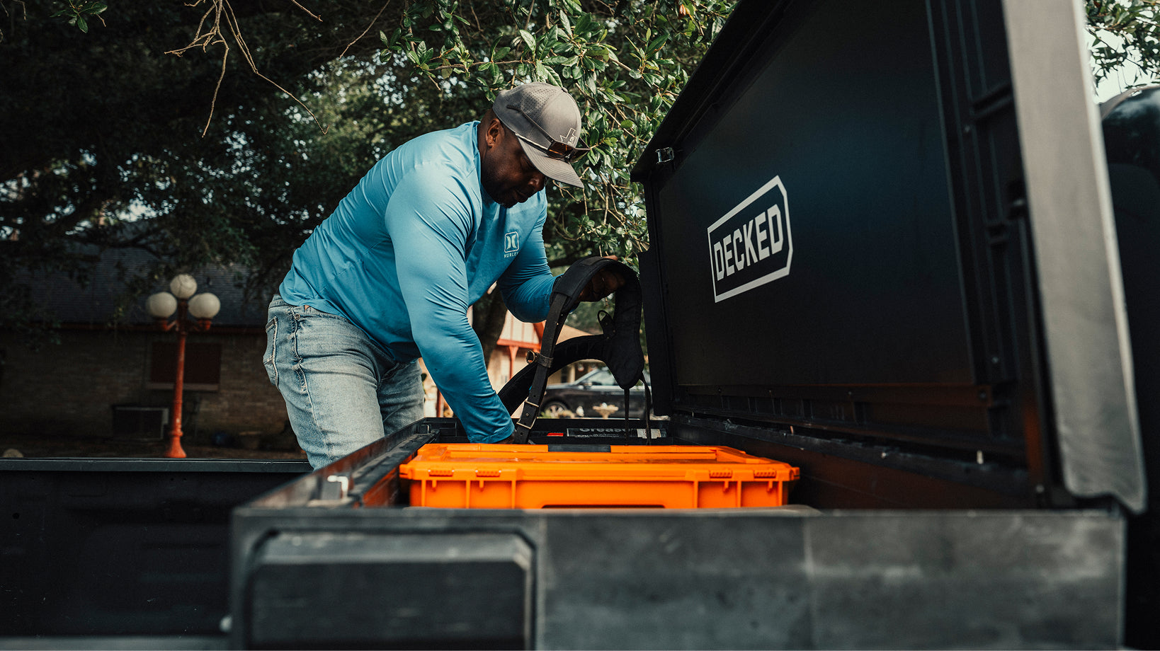 Man loading gear into his DECKED toolbox loaded with orange halfrack.