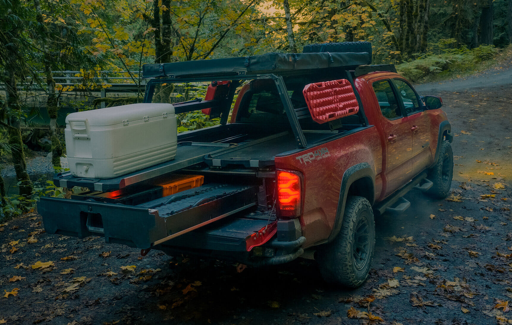 Red truck with open bed carrying a cooler on a forest road