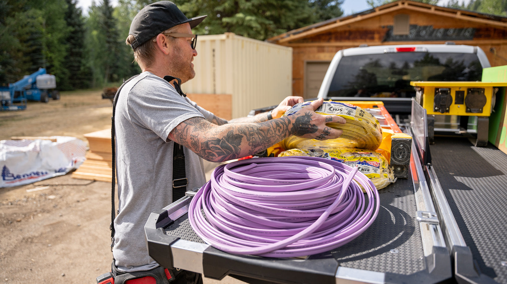 Electrician loading coiled tubing and insulation onto a DECKED CargoGlide in a pickup truck bed.
