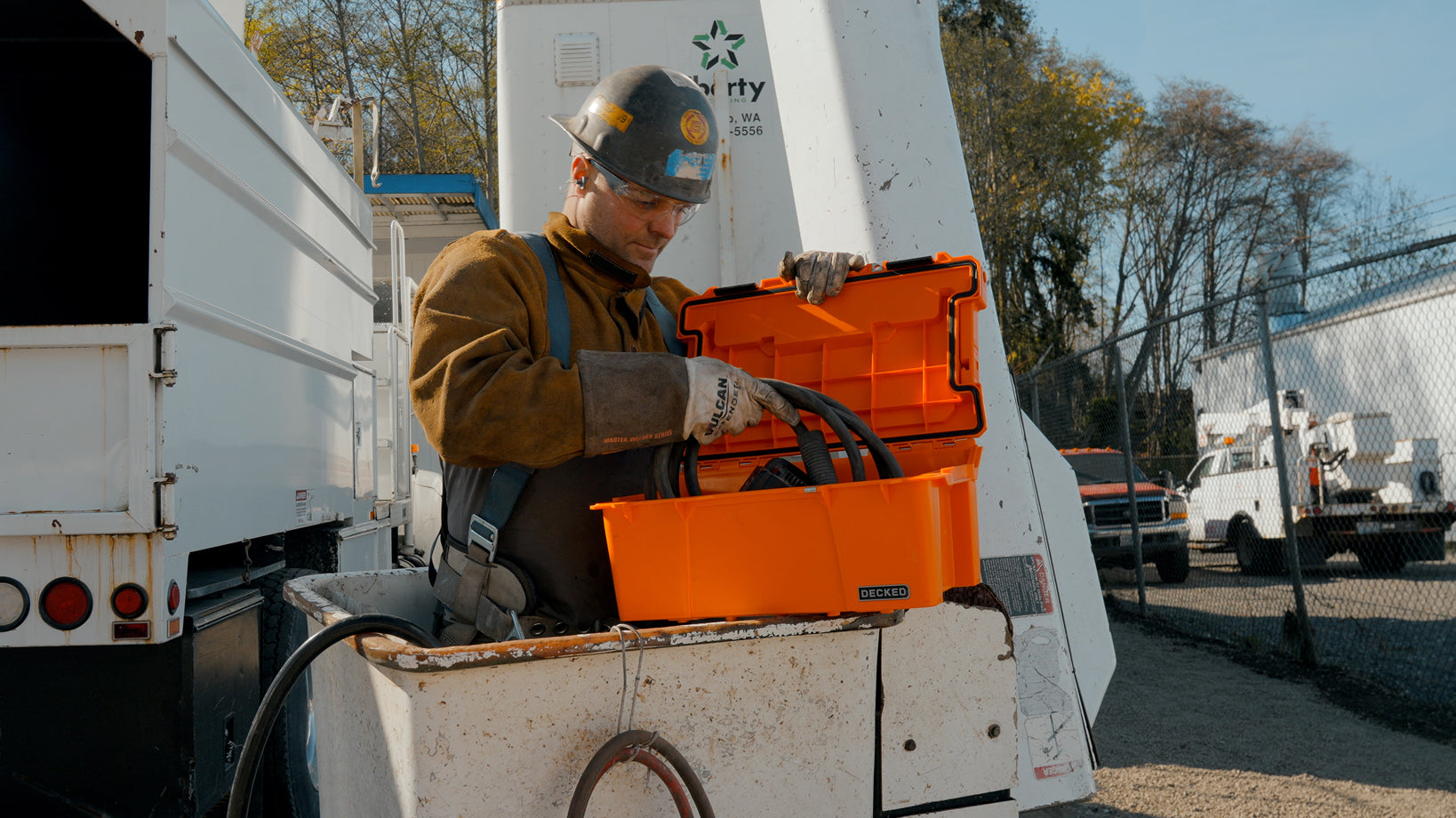 Utility worker organizing heavy-duty cables in an orange DECKED sixer beside a service truck.