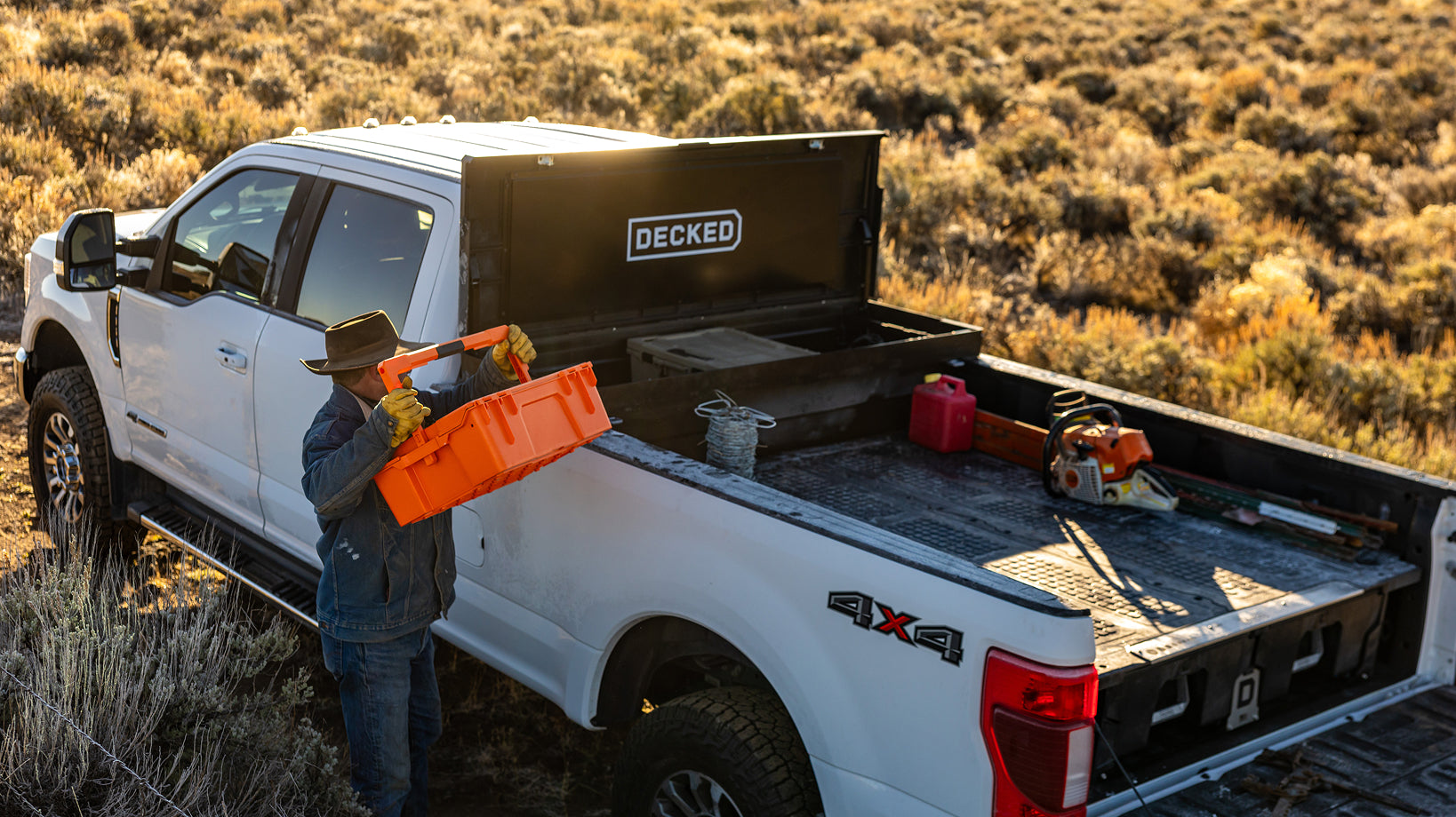 Man loading orange halfrack into a black DECKED toolbox on a ranch.