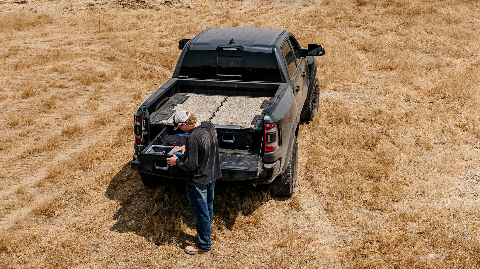 Man removing tools from a DECKED drawer system in a dry grass field.