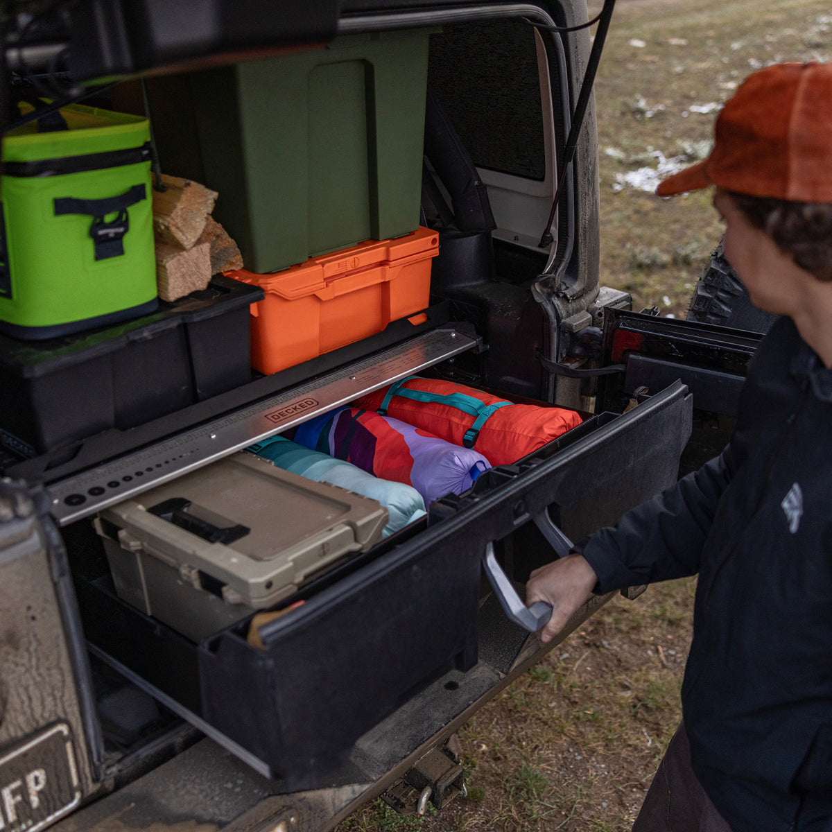 Man opening a DECKED drawer filled with camping gear in the back of a Jeep Wrangler.