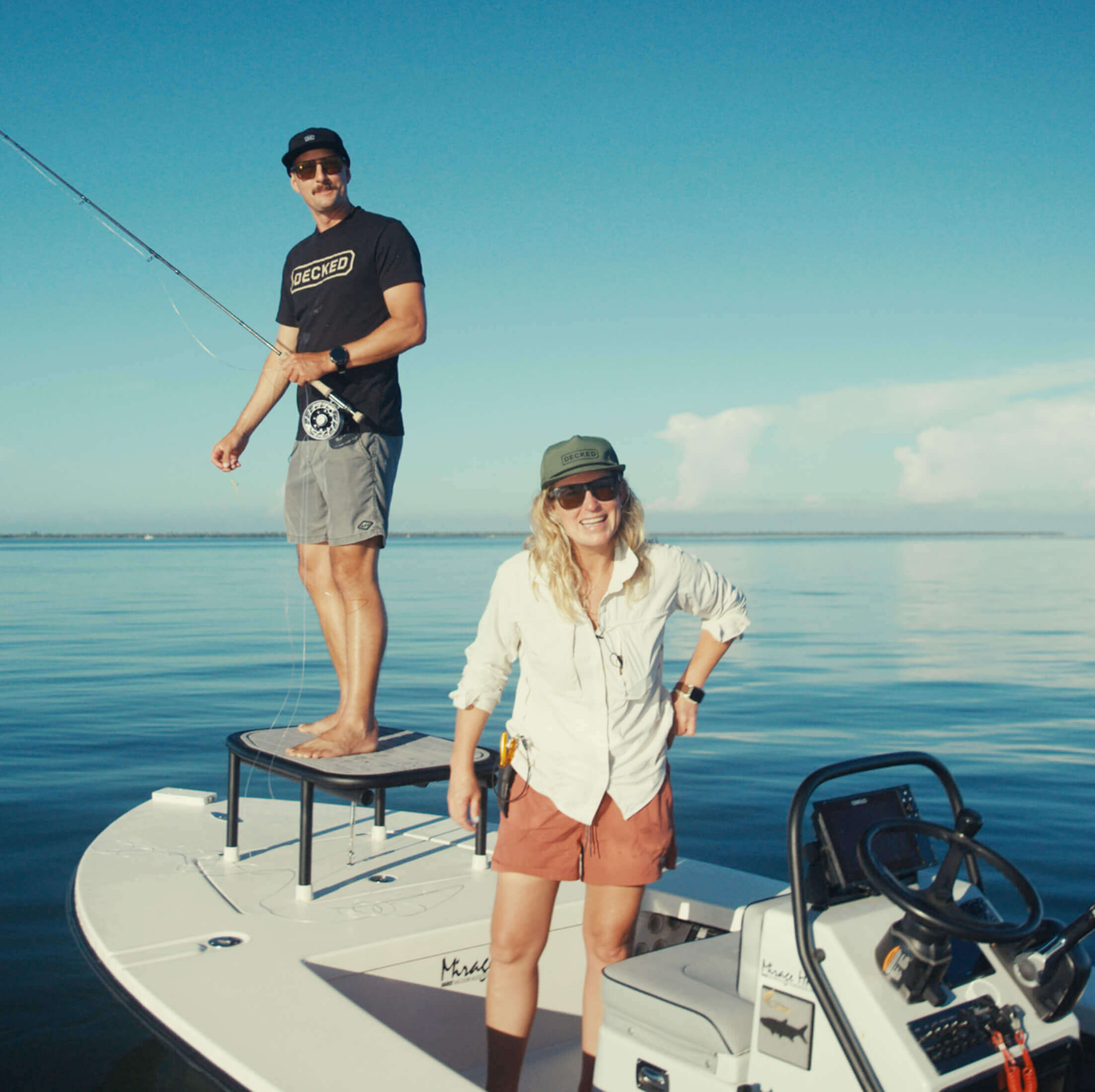 Two people on a boat in the middle of a calm blue sea with clear skies.