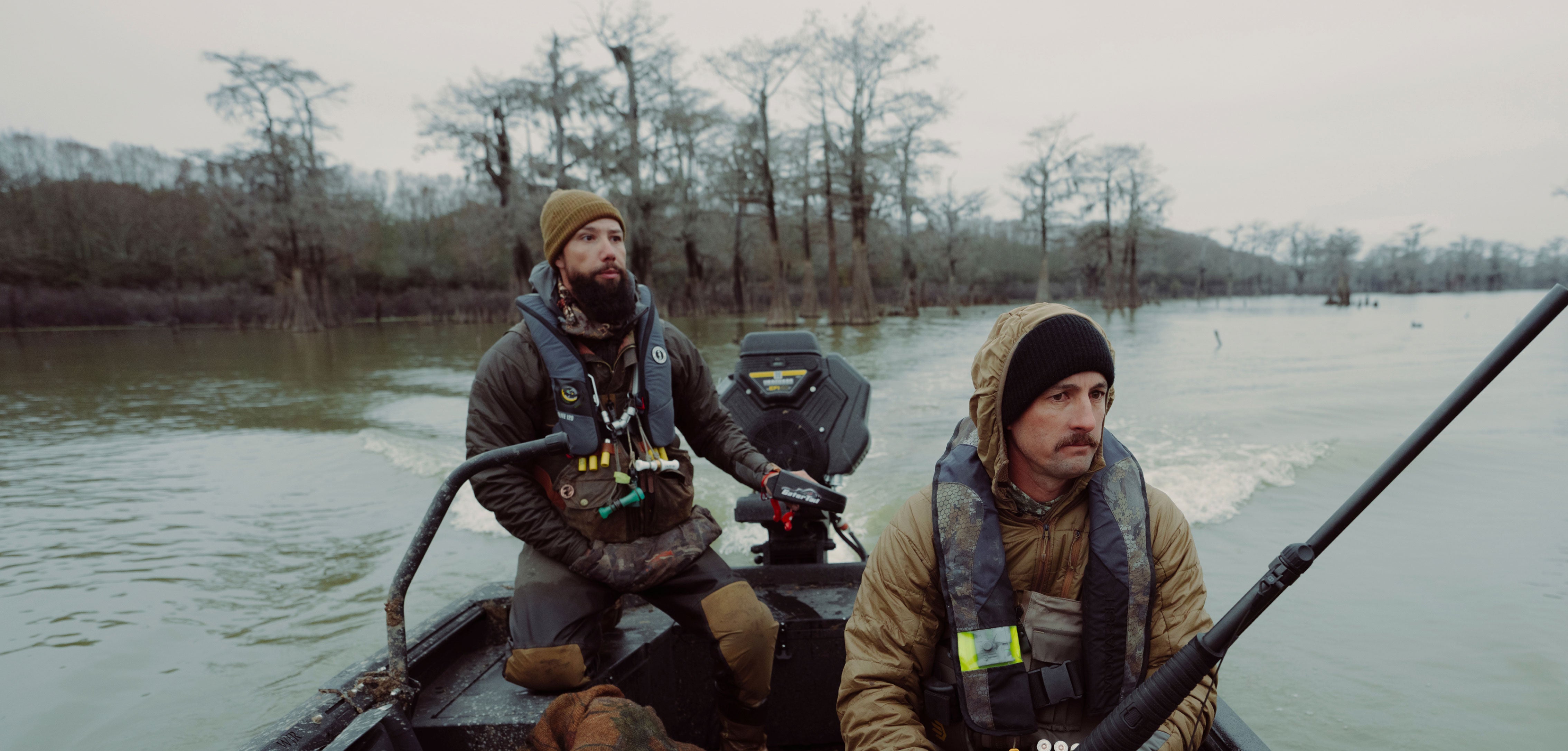 Two men in a boat on a body of water with trees in the background