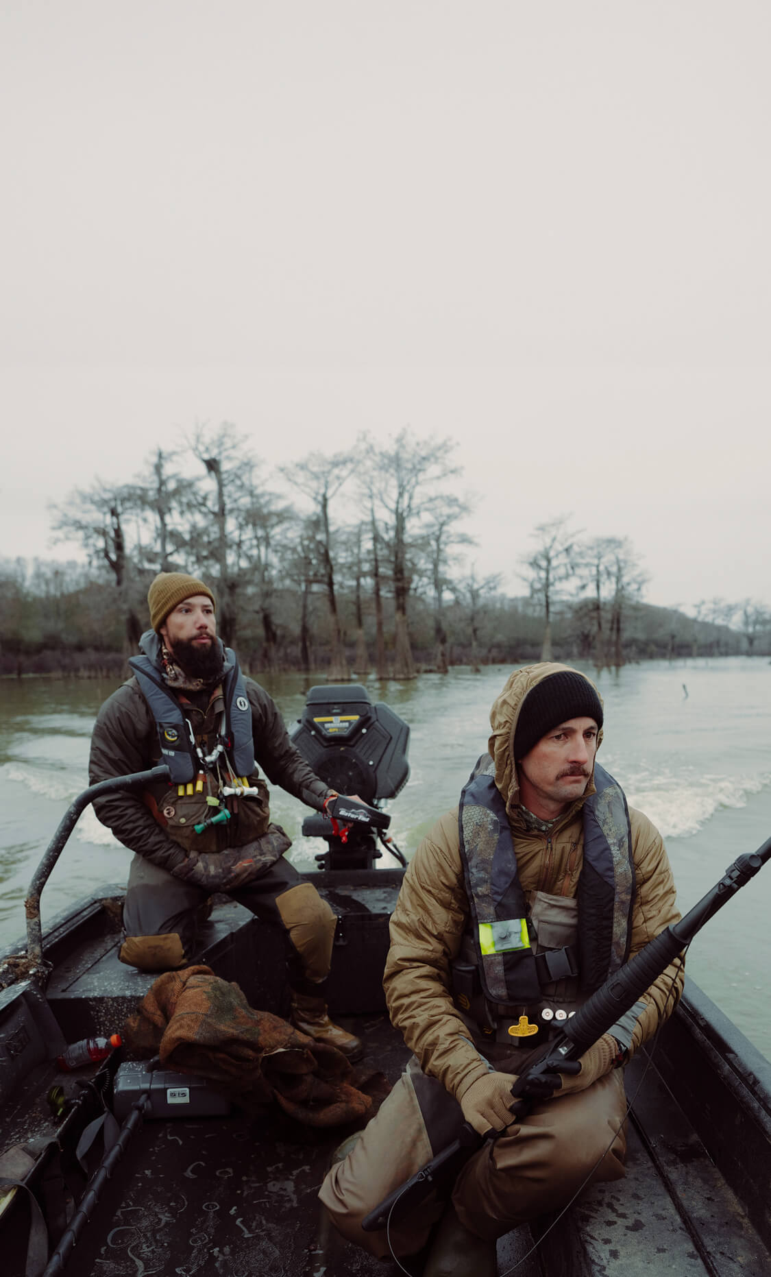 Two men on a boat in a body of water with trees in the background