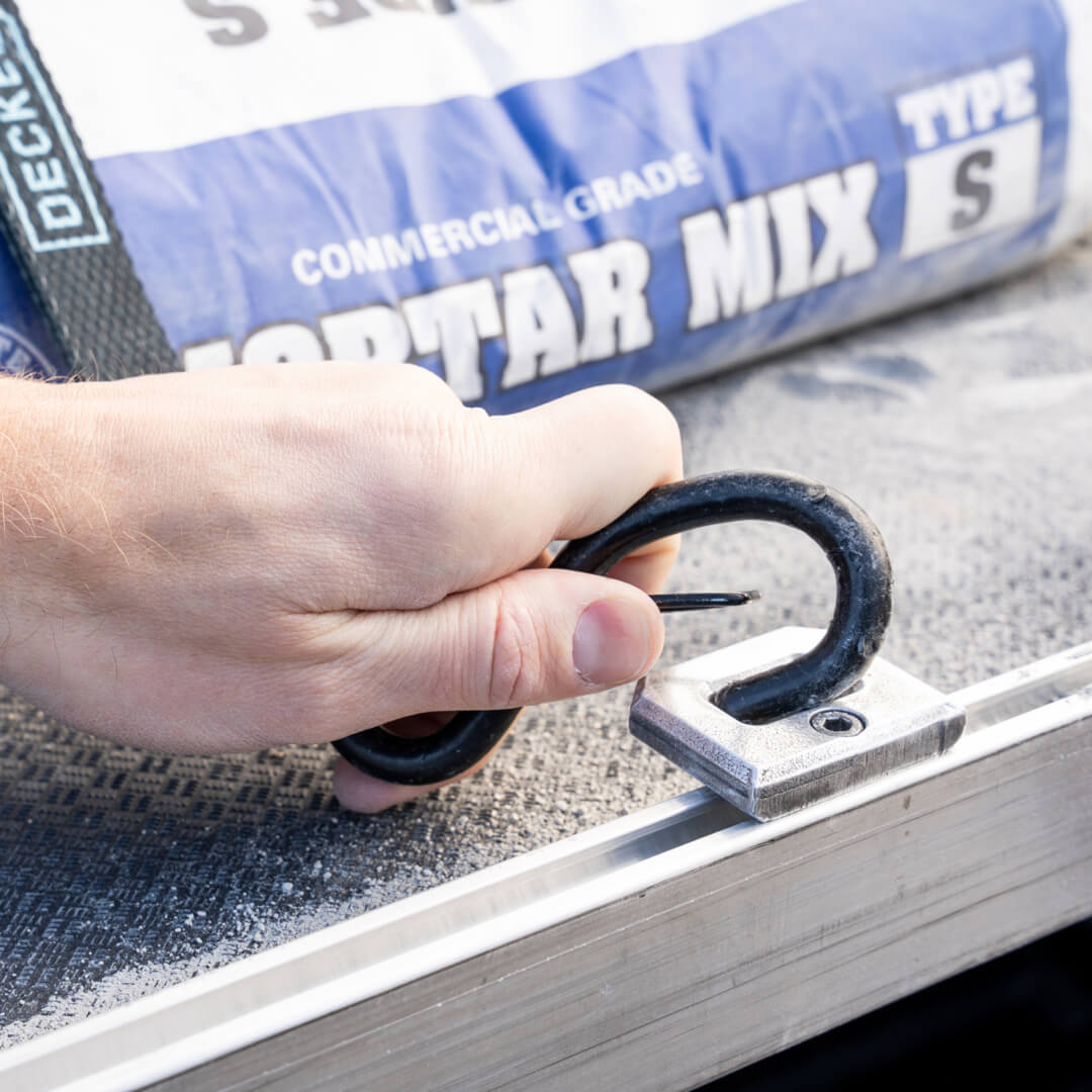 A man attaching a DECKED Cam Strap to the D-rings for CargoGlide accessory to hold down 80lb bags of mortar mix on top of the CargoGlide.