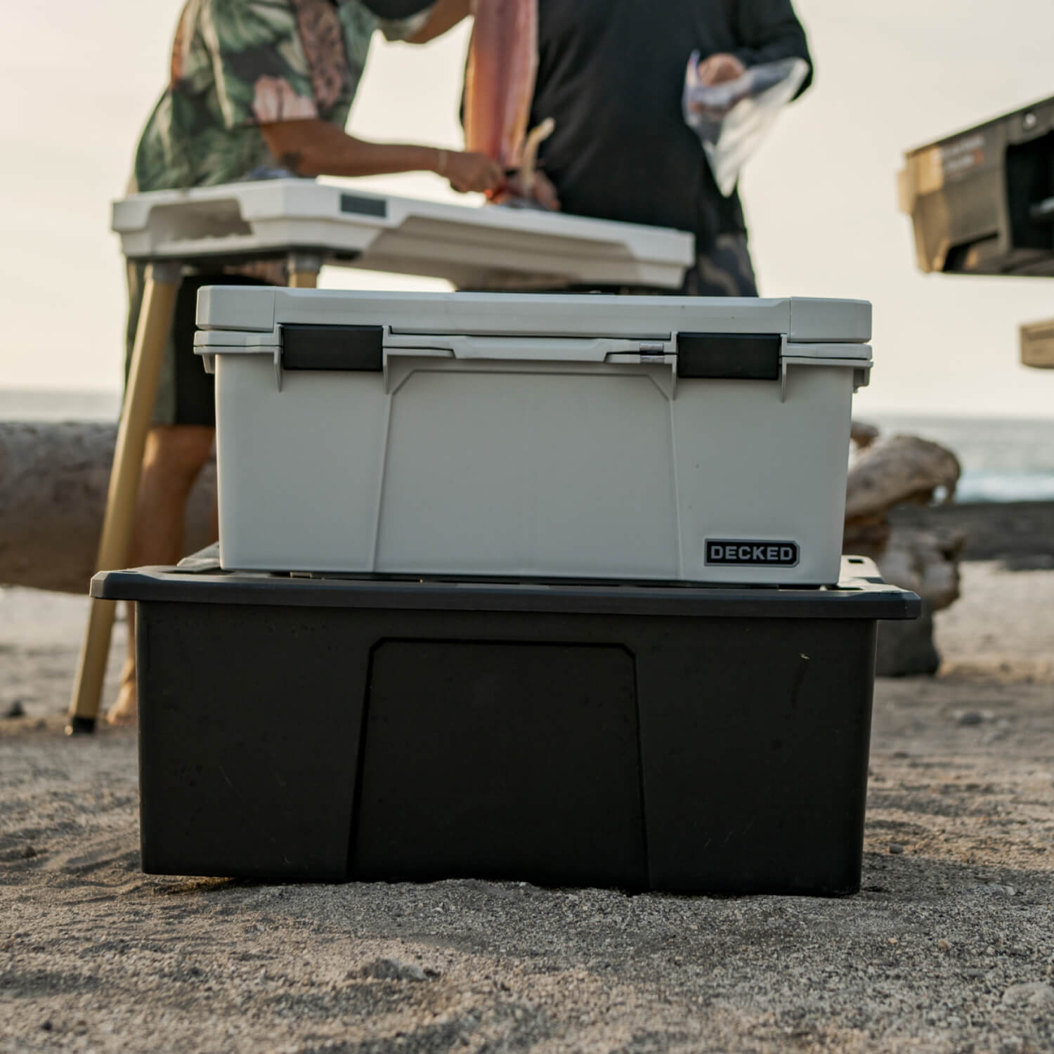 The Cool Gray Sixer stacked on top of a Payloader 32 D-co Case, in the background are some friends filleting a fish for a quick dinner on the beach.