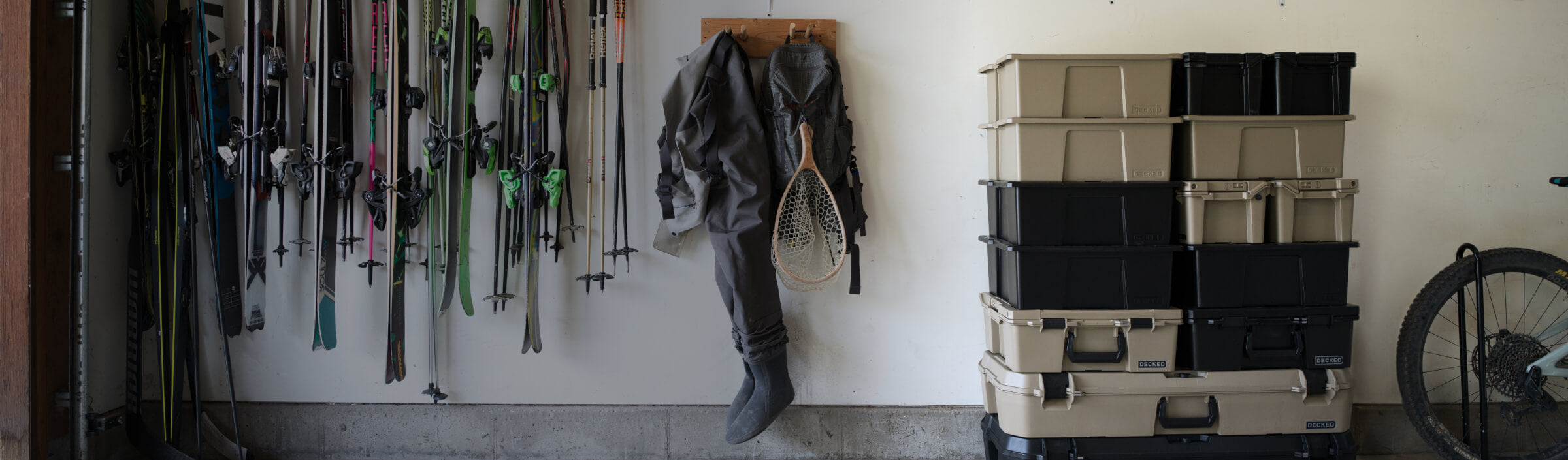 A mix of colors and sizes of D-Co Cases stacked in a garage with skis, fishing waders, and a bike sitting nearby.