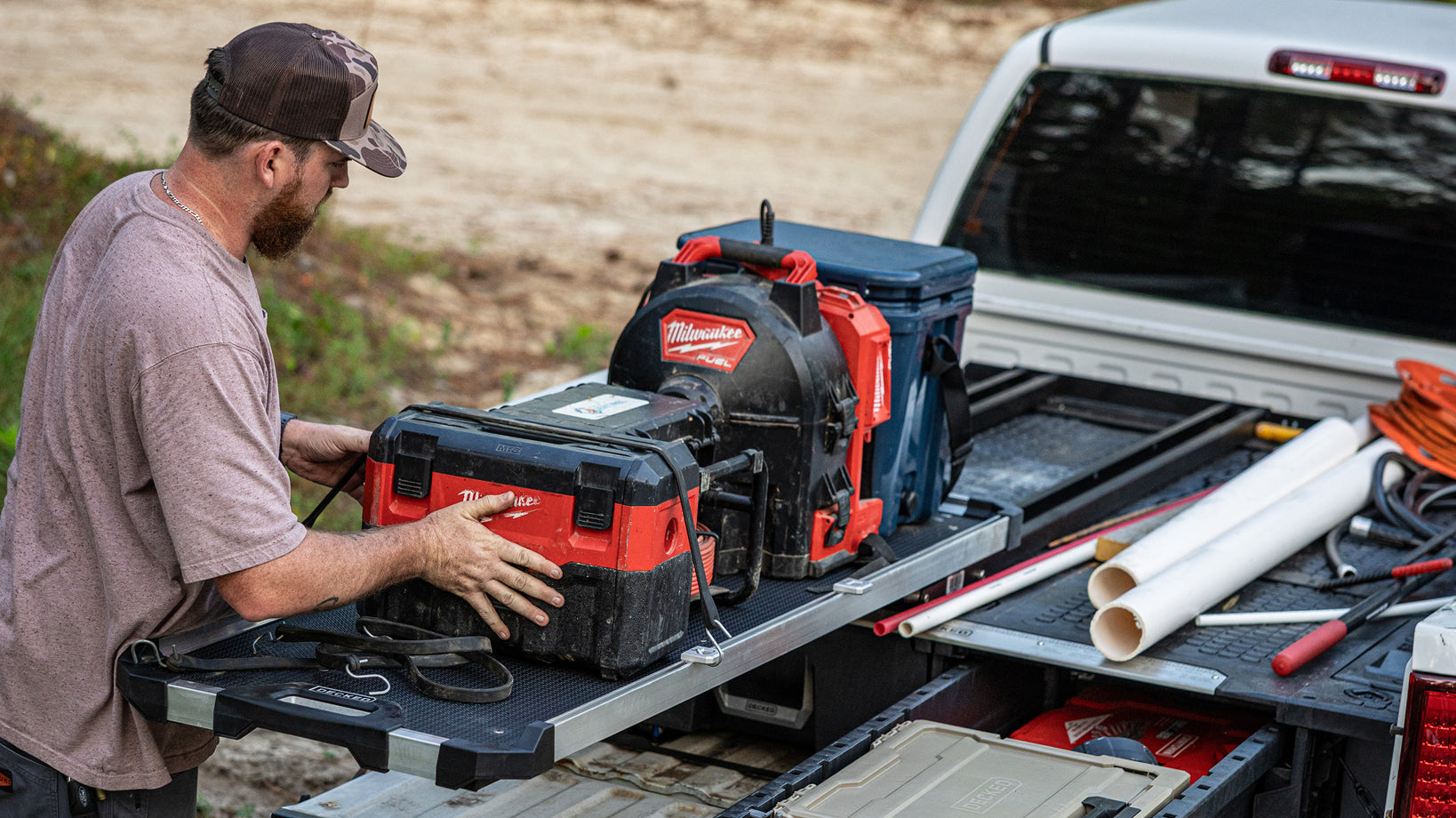 Plumber loading power tools onto a DECKED CargoGlide above a Drawer System filled with plumbing supplies.