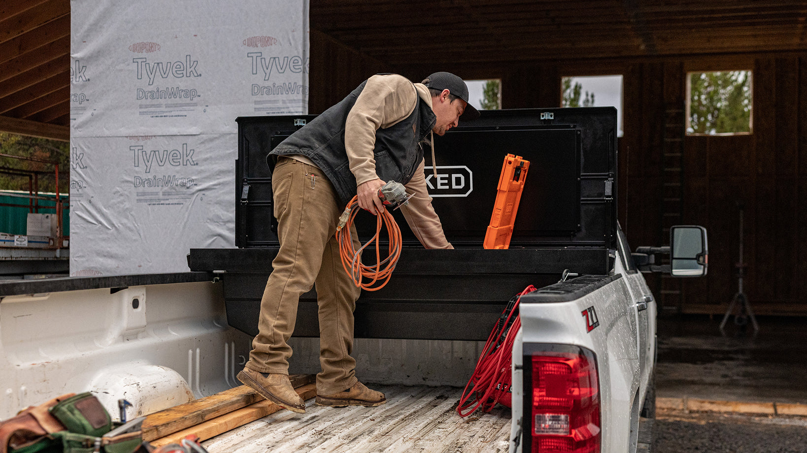 Contractor retrieving power tools and extension cords from a DECKED Tool Box at a construction site.