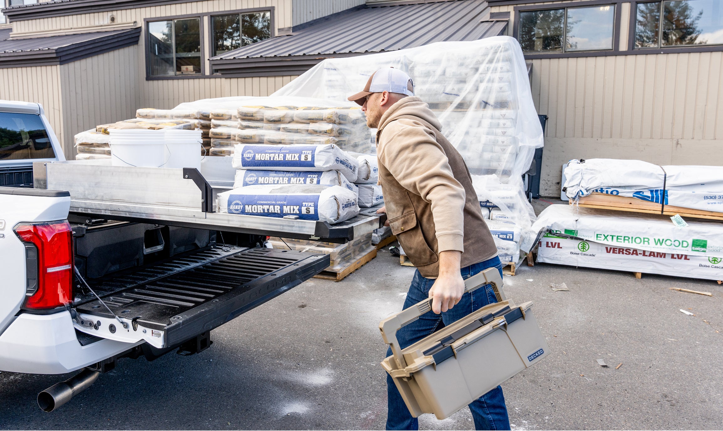 Contractor carrying a DECKED D-co Case beside a CargoGlide loaded with bags of mortar mix.