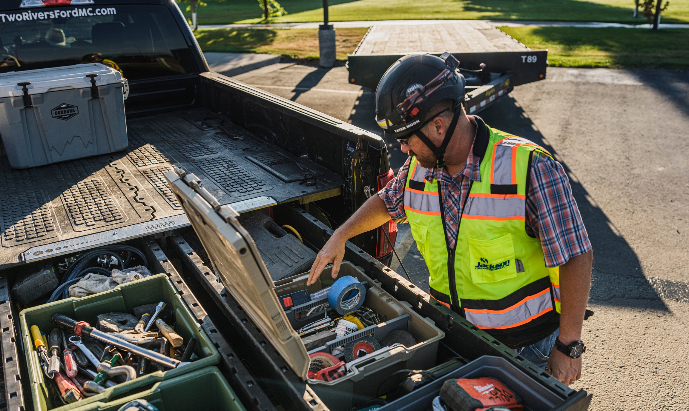 Construction worker accessing organized tools from open DECKED drawers in a pickup truck bed.