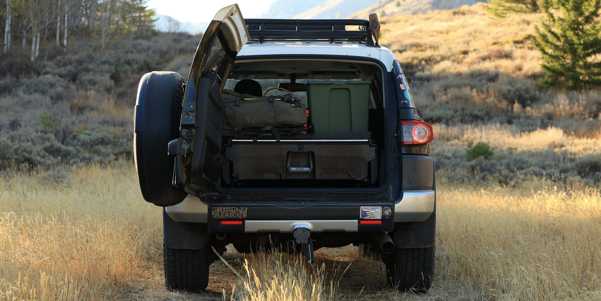 DECKED Drawer System installed in the cargo area of a Toyota FJ Cruiser parked in a grassy field.