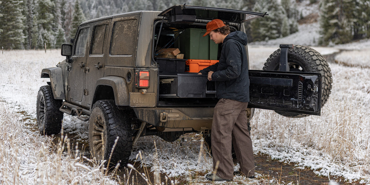Man accessing gear in the back of a Jeep Wrangler with a DECKED Drawer System in a snowy landscape.
