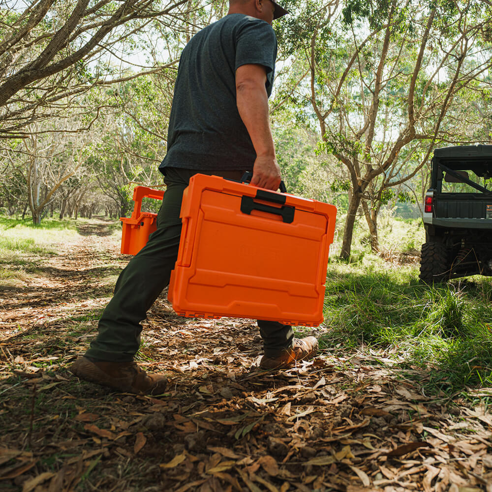 A man carrying the Blaze Orange Sixer and Halfrack D-co cases. The orange of the cases pops in the woods, making them easy to spot.