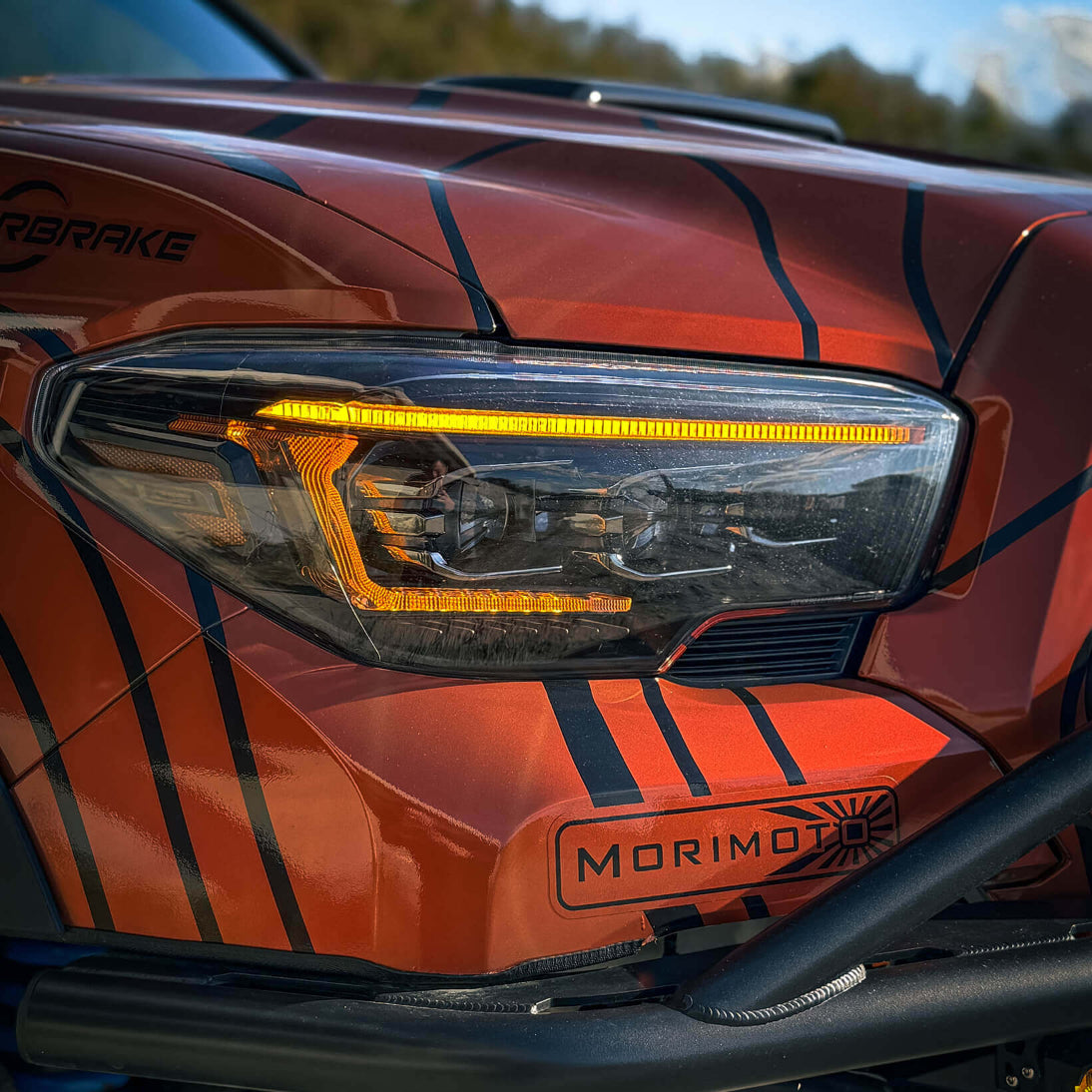 Close-up of an orange vehicle headlight with 'Morimoto' branding.