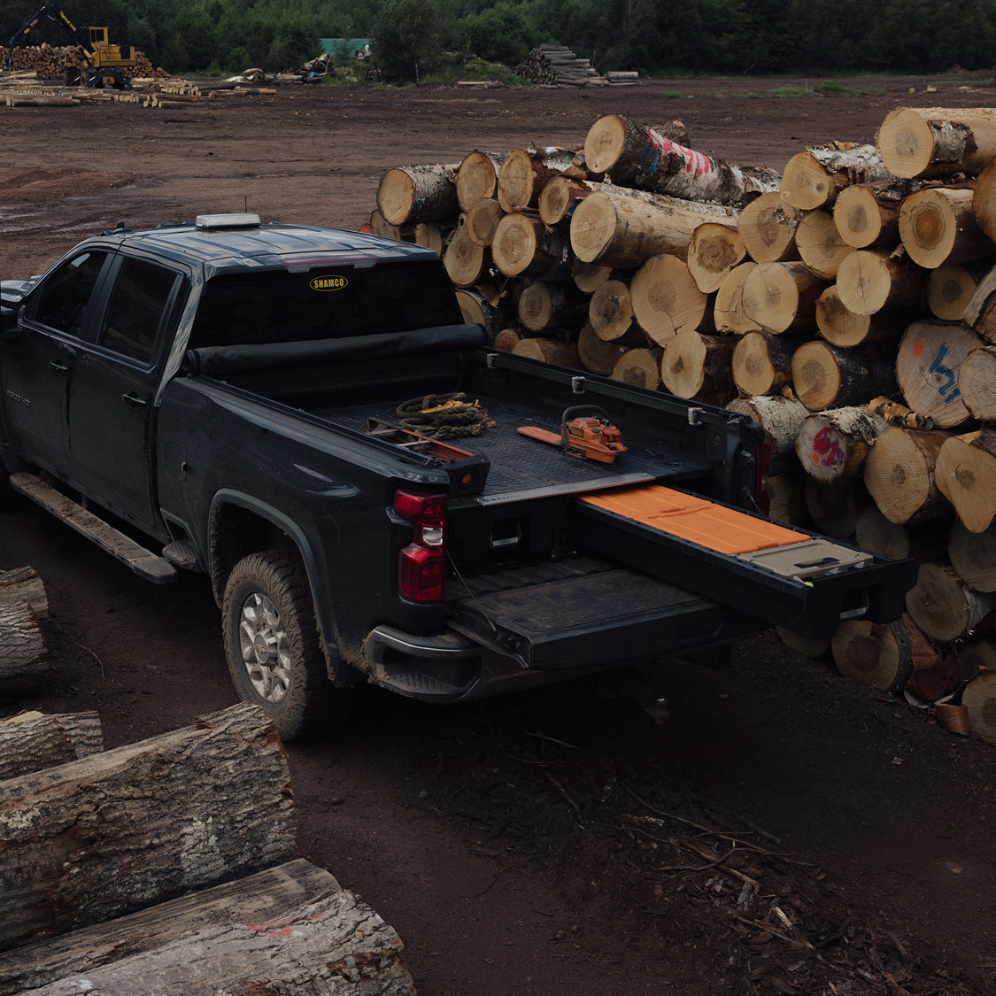 DECKED Drawer System open in a pickup truck bed surrounded by stacks of timber at a logging site.