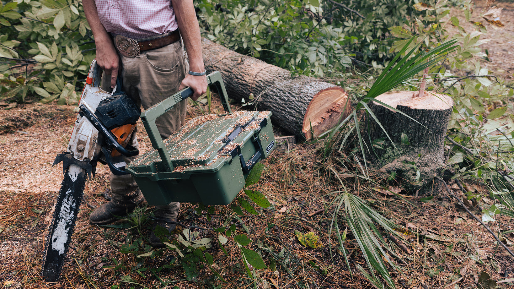 Man carrying DECKED halfrack and chainsaw at a logging site.