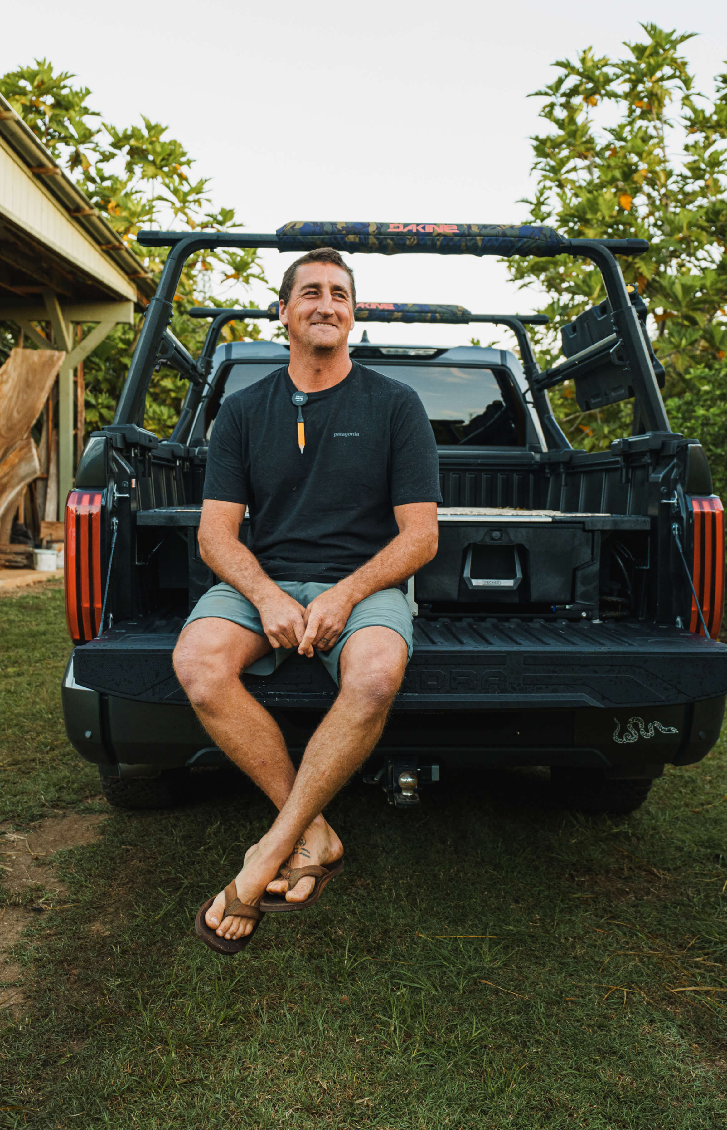 Ben Wilkinson, craftsman and big wave surfer, sitting on the tailgate of his truck, showing off his DECKED Drawer System and aussie smile.
