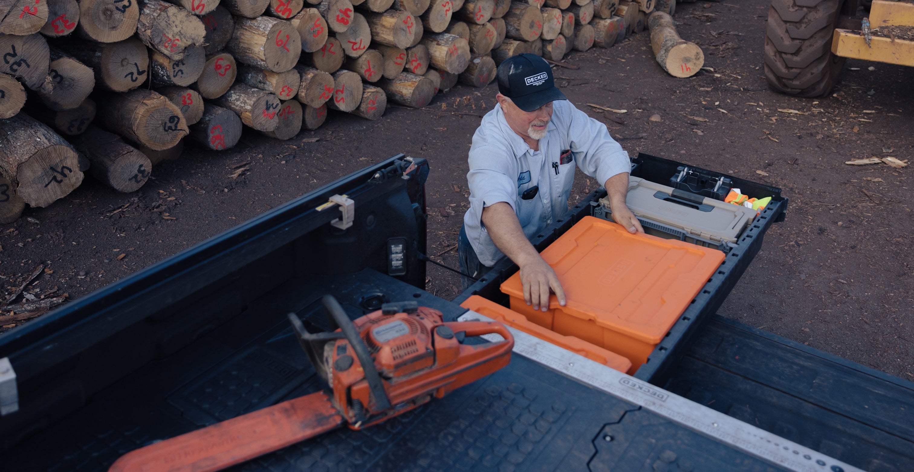 Man loading orange payloader into Drawer system with chainsaw on top at a logging site.