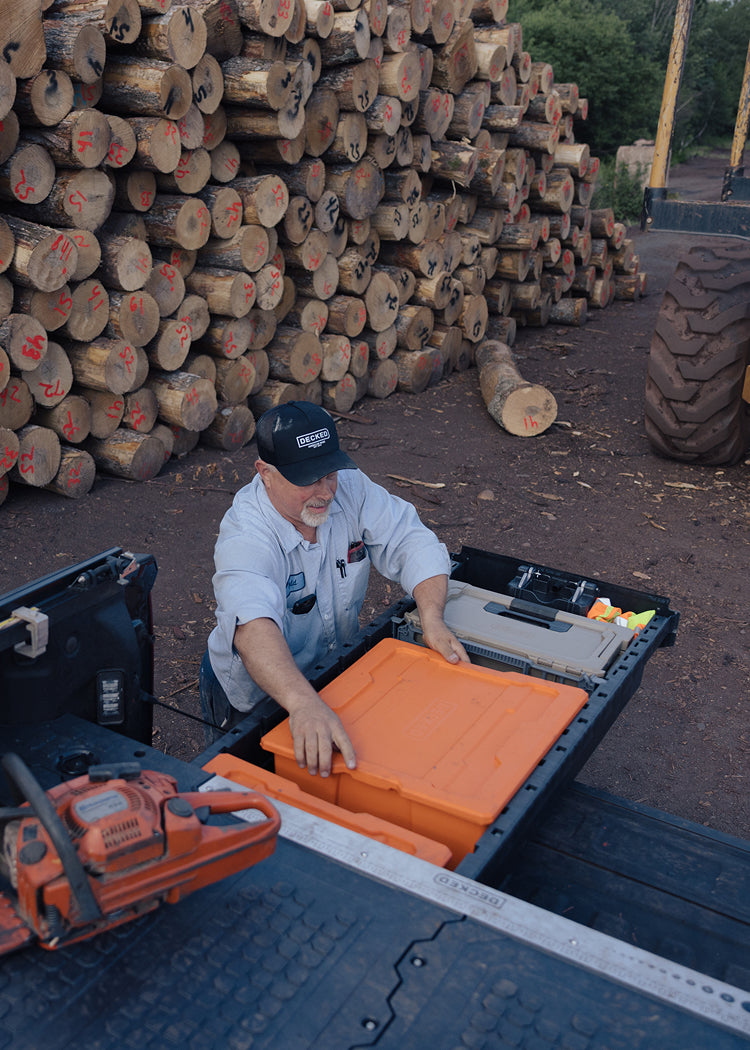 Man loading orange payloader into Drawer system with chainsaw on top at a logging site.
