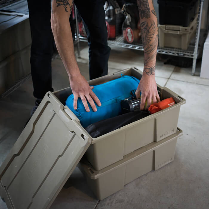 Person organizing items in a Payloader 32 storage container in a garage setting.