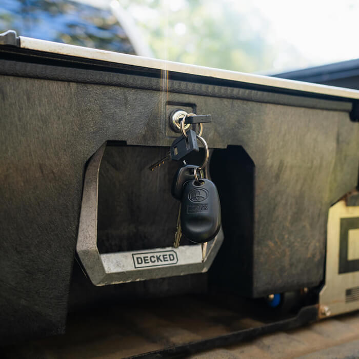 Keychain hanging from a 'DECKED' truck bed drawer lock with blurred natural background
