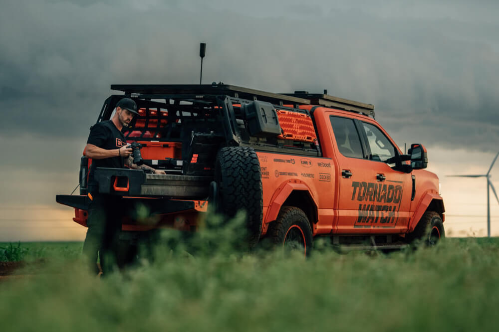 Orange truck with 'Tornado' branding parked in a grassy field.