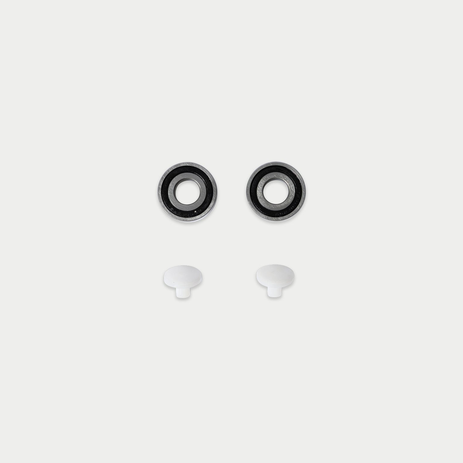 [W-DCG-CS-BEARING-KIT] A pair of black and silver skateboard bearing cups with two small white plastic caps below them, arranged symmetrically on a light gray background.