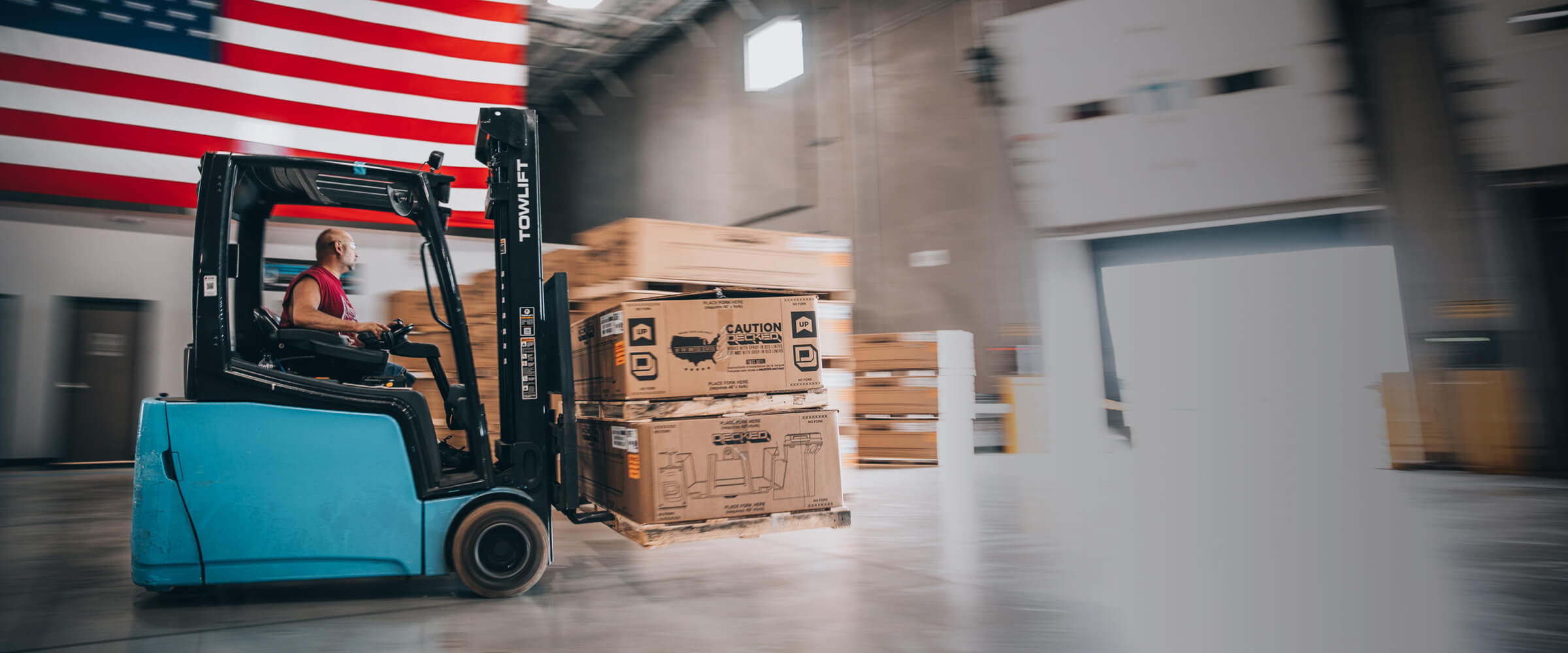 Blue forklift driving through a factory carrying DECKED boxes