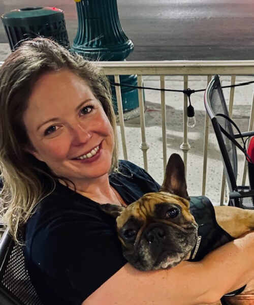 Breann smiling with her pup, a brown and black Frenchie.