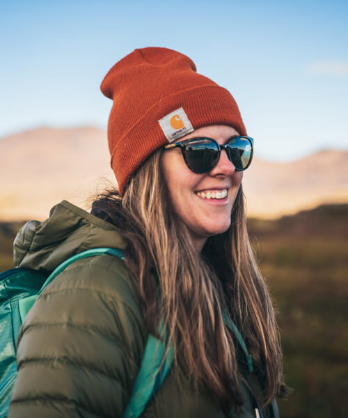 Bridget smiling in a stylish beanie, sunnies, and a puffy coat looking like she is off to somewhere cool.