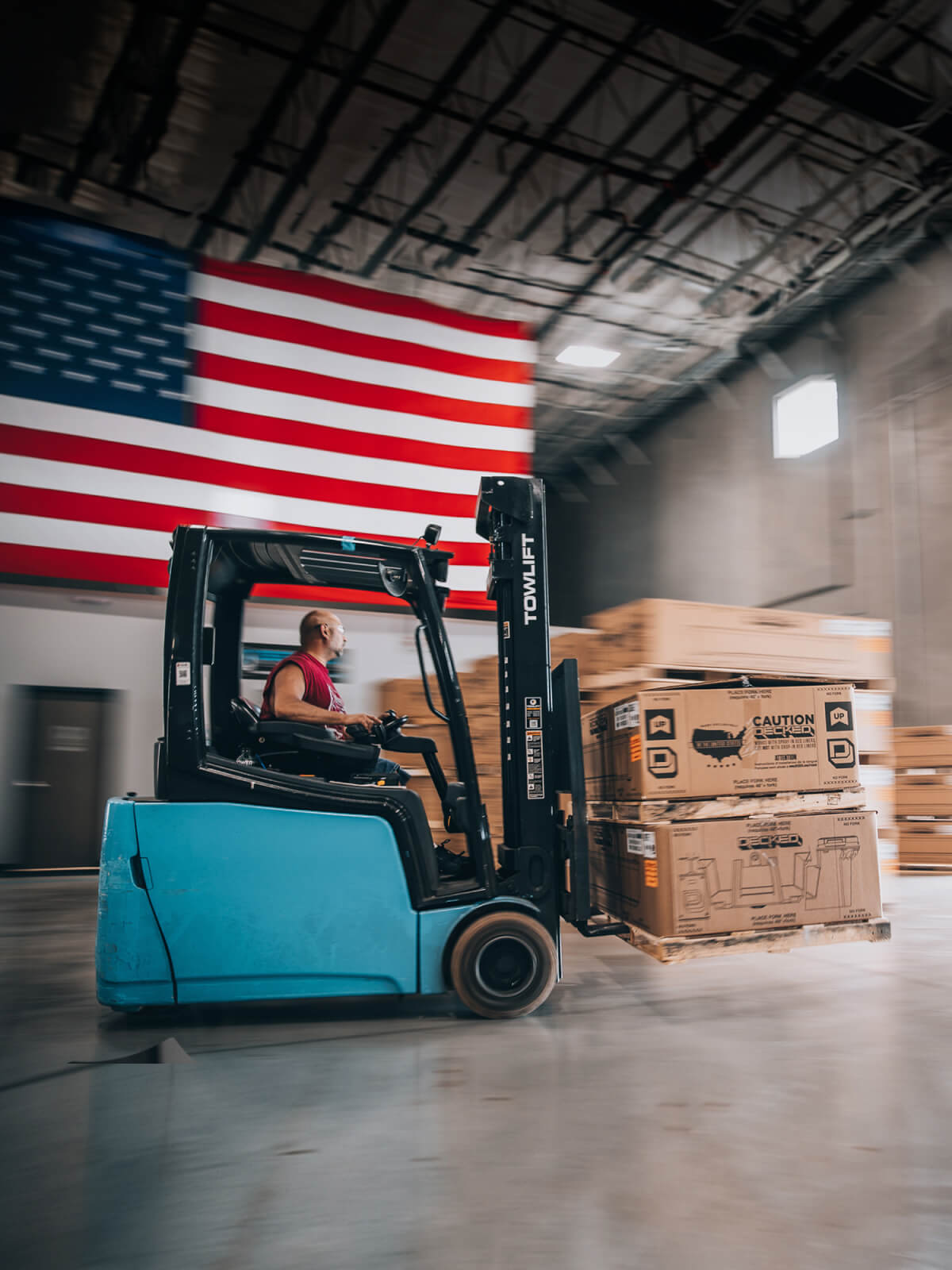 Blue forklift driving through a factory carrying DECKED boxes