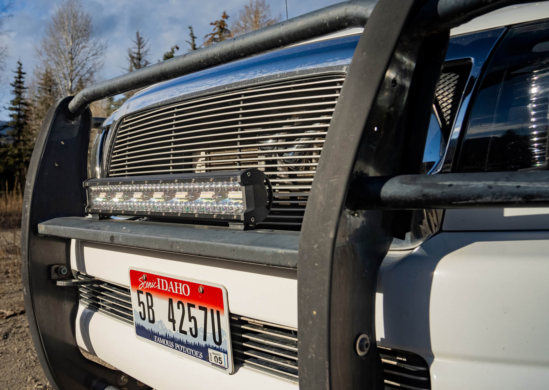 Close-up of a vehicle's front bumper with a license plate and light bar, set against a natural background.