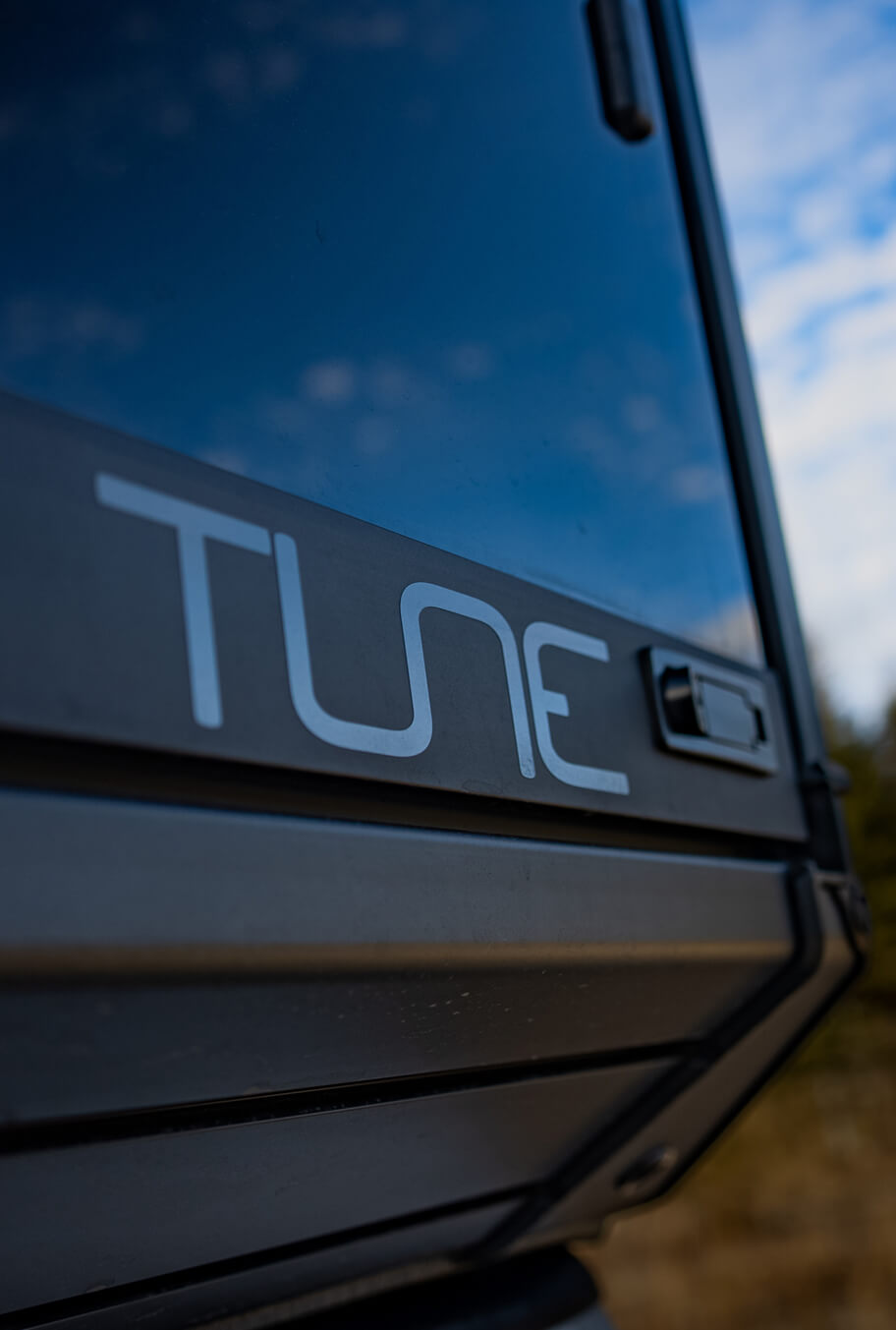 Close-up of a vehicle window with 'TUNE' decal against a blurred natural background
