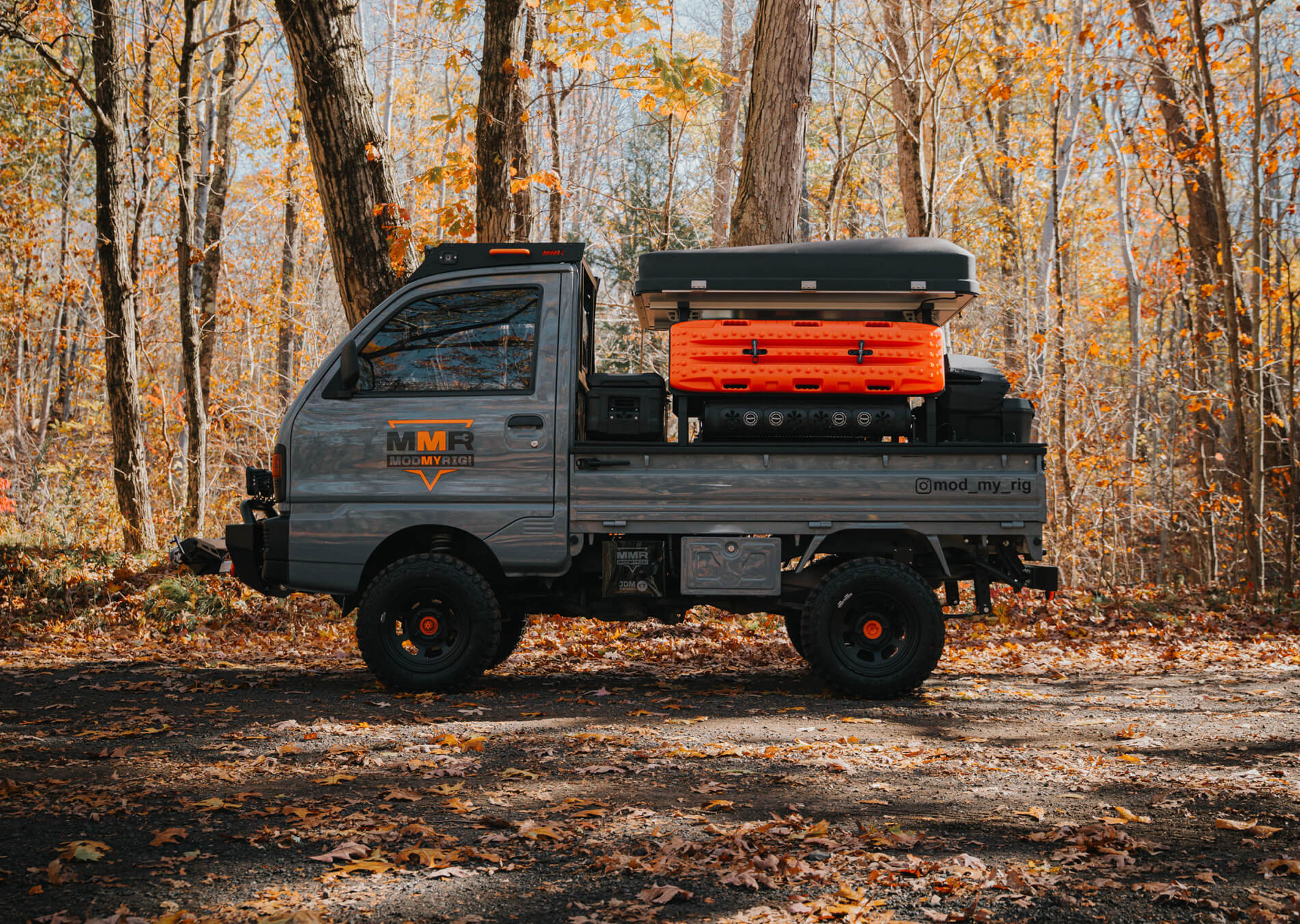 Small truck with a flatbed and orange toolbox in a forest setting