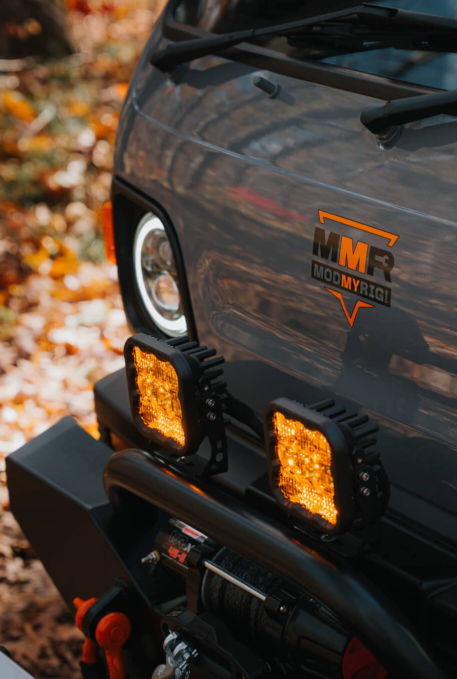 Close-up of a vehicle's front with visible branding and lights, set against a natural background.